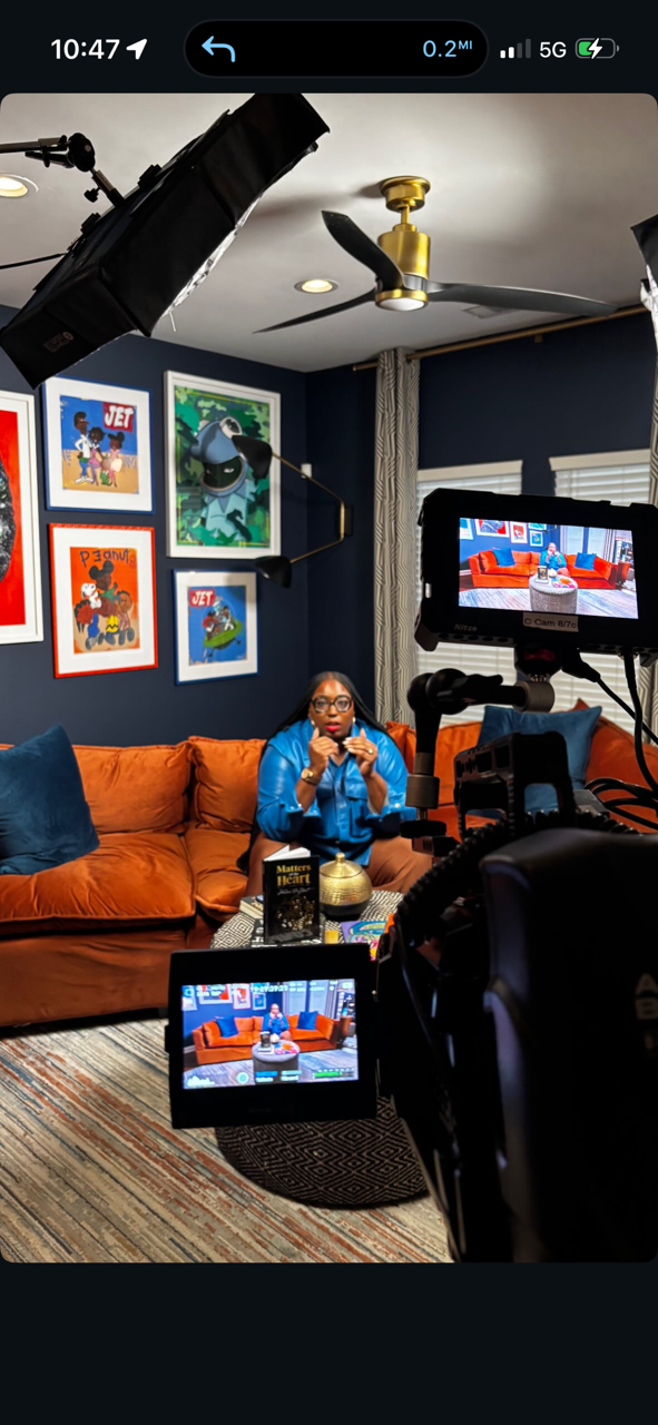 Madam Prezident on set in blue leather, orange velvet sofa, navy walls, JET prints